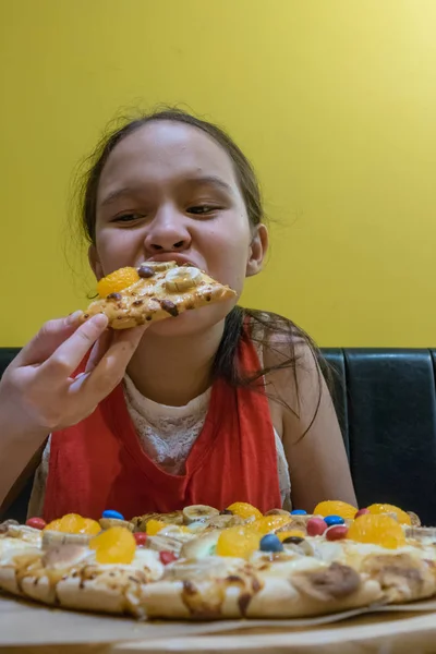Young mixed race tween girl eating candy, marshmallow, and chocolate pizza