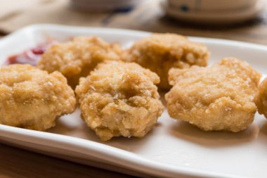 Altın kızarmış tavuk nuggets arka planda domates soslu beyaz plaka üzerinde