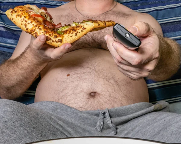 Fat man eating pizza and using TV remote