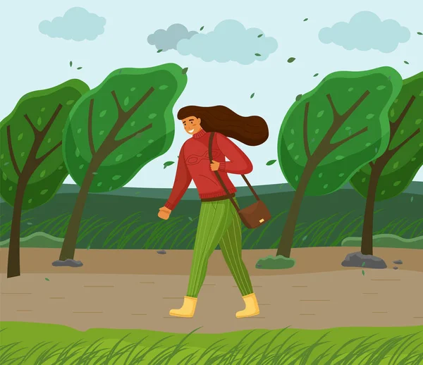 Winderig weer, vrouw loopt in het park door harde wind, groene bomen buigen, bladeren vliegen in de lucht — Stockvector
