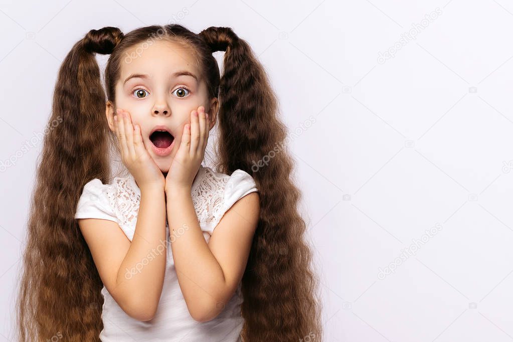 Little amazed girl opened her mouth, palms on cheeks at white background