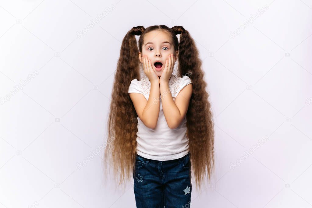 Little amazed girl opened her mouth, palms on cheeks at white background