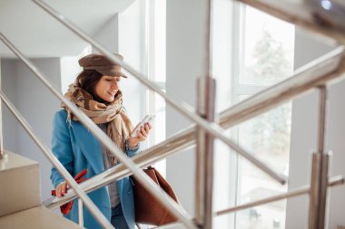 Paltolu iş kadını alışveriş merkezindeki merdivenleri yükselir. Alışveriş. Moda