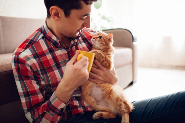 Jeune homme tenant un chat et buvant du thé à la maison — Photo