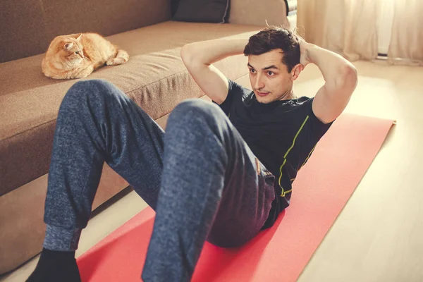 Evde kediyle yerde spor yapmak için bir adam gidiyor. Basını sallar.