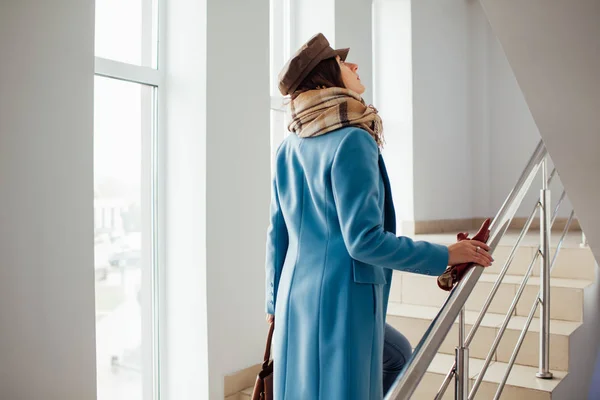 Business woman in coat rises the stairs in the mall. Shopping. Fashion