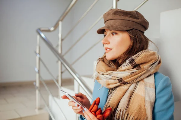 paltolu iş kadını akıllı telefon ile alışveriş merkezinde merdivenlerde duruyor. Alışveriş. Moda