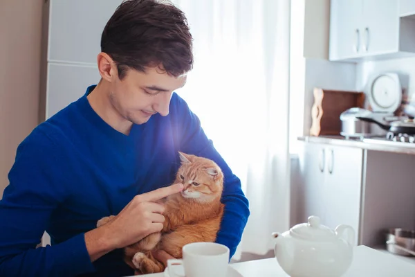 Portrait de beau jeune homme jouant avec le chat dans la cuisine — Photo