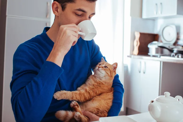 mutfakta bir kedi ile çay içen genç bir adamın portresi