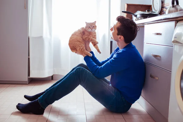 Jeune homme assis sur le sol de la cuisine avec un chat — Photo