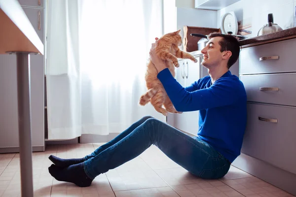 Jeune homme assis sur le sol de la cuisine avec un chat — Photo