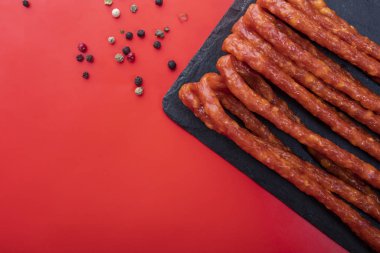 Kuru sosis. Kırmızı arka planda baharatlarla ince sosis