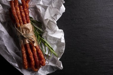 Koyu bir arka plan üzerinde sarımsak ve otlar ile ince sosis