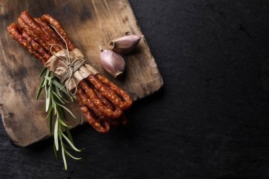Koyu bir arka plan üzerinde sarımsak ve otlar ile ince sosis