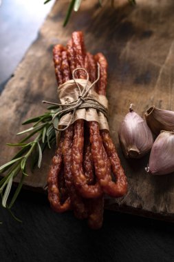 Koyu bir arka plan üzerinde sarımsak ve otlar ile ince sosis