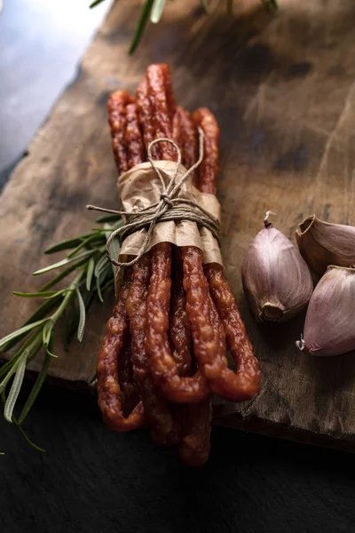 Koyu bir arka plan üzerinde sarımsak ve otlar ile ince sosis