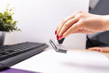 Ofisteki kadın. Kırmızı tırnaklı bir kadın eli, belgeleri kauçuk damgayla damgalar.. 