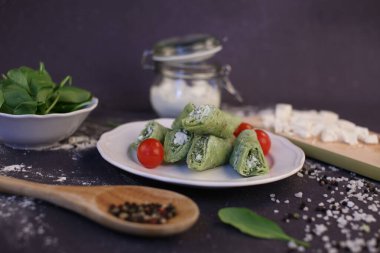 Ispanak ve peynirle doldurulmuş yeşil krep. Koyu bir arkaplanda kompozisyon