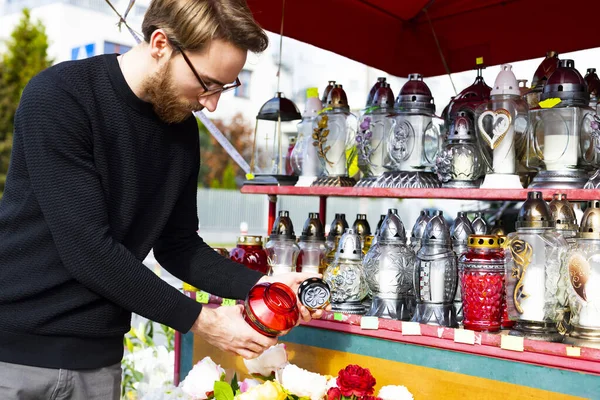 Man chooses and buys grave candles in a shopping stand next to a cemetery. All Saints Day, All Hallows Day.