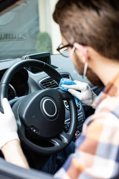 Homem de luvas de proteção e máscara facial limpando um volante. Auto detalhamento. Limpeza interior do carro . — Fotografia de Stock