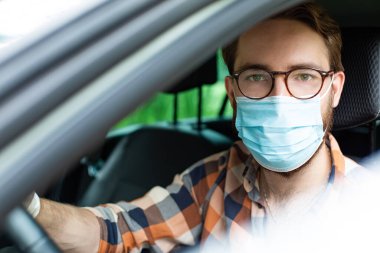 Koruyucu eldivenleri ve maskesiyle arabada oturan bir erkek sürücü. Enfeksiyon ve virüslere karşı her gün önleme. 