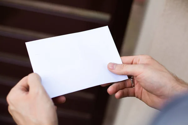 Male hands holding a letter, envelope with a copy-space, close up, focus on letter. Sending, receiving, mail, postcard, message. Traditional mail, correspondence. Postman. Checking a letterbox.