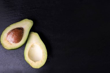 Olgun, yarım avokado, siyah, taşlı arka plan, fotokopi alanı ve metin alanı olan üst manzara. Vejetaryen, çiğ yemek. Lezzetli sağlıklı sebzeler. Diyet konsepti, yemek kompozisyonu.