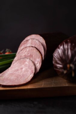 Kuru, tütsülenmiş, tahta kesme tahtasında Krakowska sosisi ve siyah taşlı bir atölye. Et salatası konsepti, dilimlere odaklan. Klasik Krakowska sosisi, Polonya lezzeti.. 