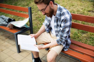 Sakallı genç bir adam bir bankta oturuyor, kitap okuyor, bir rehber. Sırt çantalı ve haritalı şehir gezgini Polonya, Avrupa 'da açık havada dinleniyor, otobüs, ulaşım beklerken kitap okuyor.