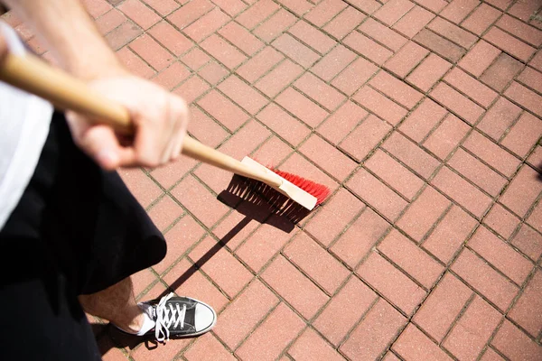 Sweeping outdoor. Cleaning the driveway, stone paving with a broom, a sweeper. Cleanup works around the house on a sunny day.