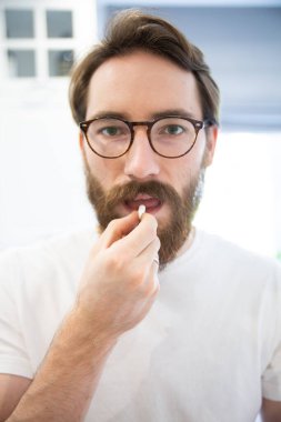 Beyaz tişörtlü, hap içerken kameraya bakan sakallı bir adamın portresi. İlaçlar, ilaçlar, vitaminler almak.