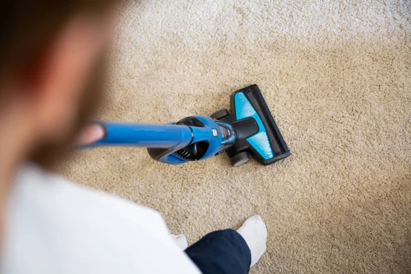 Top view of vacuuming a carpet with a blue portable, cordless handheld vacuum cleaner. Keeping house clean.