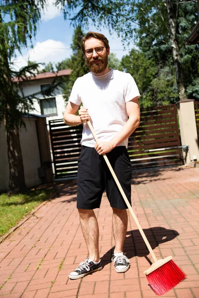 Sweeping. Man cleaning a driveway in front of a propertys entrance gate, with a broom.