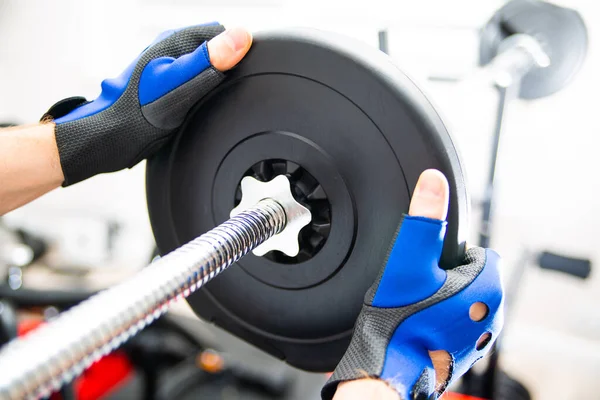 Male hands loading weight plates on a barbell, focus on a plate. Heavy weight exercise.