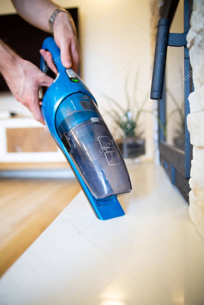 Vacuuming house with a handheld vacuum cleaner.
