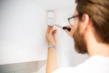 Beyaz, plastik bir alarm sensörünü tamir etmenin yatay görüntüsü, tornavidayla dedektör. İş sırasında tamirci, ev onarımı, koruma alarm sistemi onarımı..