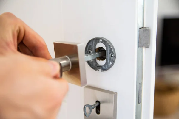 A broken metal handle in a wooden door during repairing by a handyman, close up. Small repairs of a household.