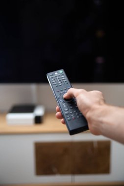 Erkek elinde uzaktan kumanda. Televizyon açmak için uzaktan kumandada bir düğmeye basmak, bulanık arkaplan ve kopyalama alanı ile dikey görünüm.