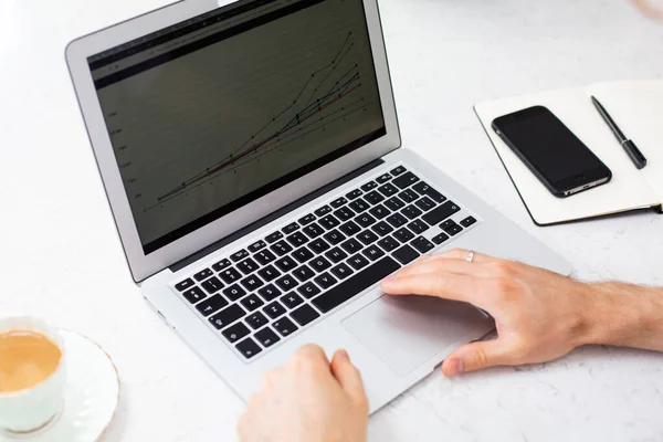 Modern, bright home office workspace with thin laptop, cell phone, notebook, coffee on a white desk. Using a mobile computer to work, prepare presentation, charts. Office working space concept.