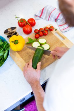 Yemek ve salata için tahta kesme tahtasında sebze kesmenin en iyi manzarası. Parlak bir mutfakta tezgahta sebze kesen bir adam. Sağlıklı vejetaryen yemeği hazırlıyorum. Sağlıklı yaşam tarzı, diyet.