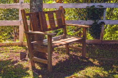 Sıcak bir öğleden sonra ağacın yanında ahşap bir bank. Arkada bir çit var..