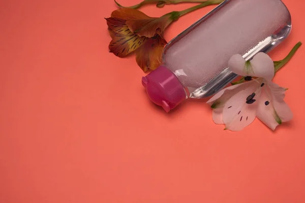 Kosmetikflasche mit Blüten, Reinigung und Make-up entfernen, Draufsicht, pastellfarbener Hintergrund, minimalistisch. — Stockfoto