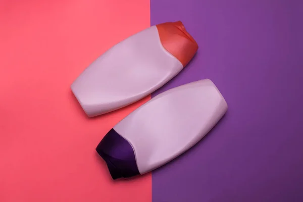 Beauty, decorative cosmetics bottles. Pink and purple colors background, flat lay, top view, minimalistic pop-art style