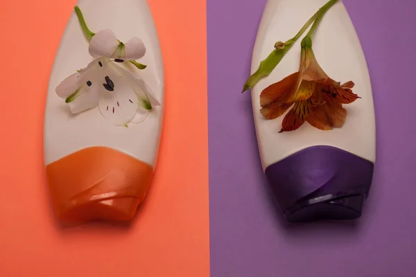 Flowers and beauty, decorative cosmetics bottles. Peach and purple colors background, flat lay, top view, minimalism.
