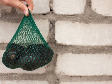 Taze organik hass avokado bir tuğla duvar arka plan, sağlıklı gıda, kopya alanı erkek ellerde yeşil bir dize çanta içinde.