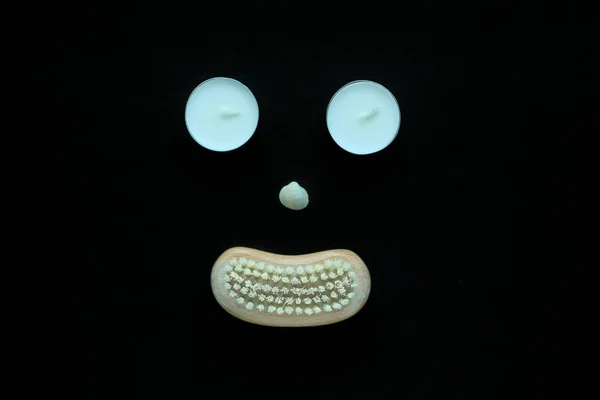 Spa Wellness concept, gezicht met ogen kaarsen, een zeeschelp neus en een mond van een houten lichaam borstel op zwarte achtergrond. — Stockfoto
