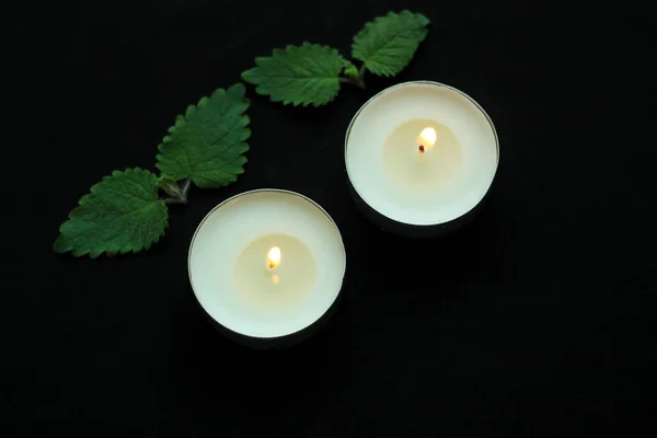 White burning tealight candles on black background. Beauty, SPA treatments, massage therapy and relax concept.
