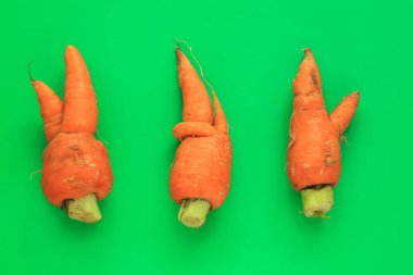 Çirkin yemekler. Yeşil ve turuncu duoton pastel arka plan üzerinde deforme organik havuç.