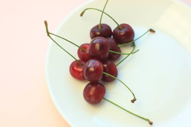 Toz pembe arka plan yakın çekim beyaz plaka üzerinde Taze soğuk kırmızı kiraz. Kopyalama alanı, minimalist stil.