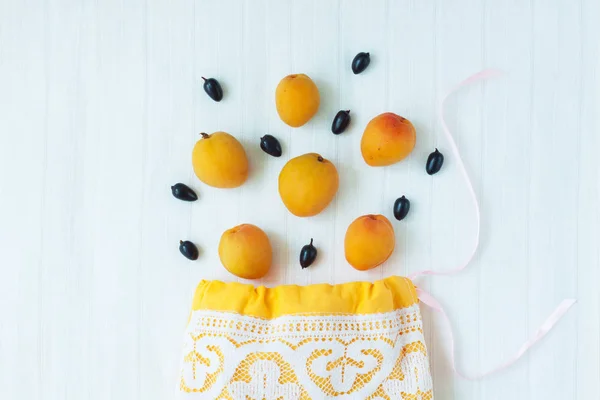 Top view of yellow cotton shopping bag with organic eco apricot fruits on white linen background.